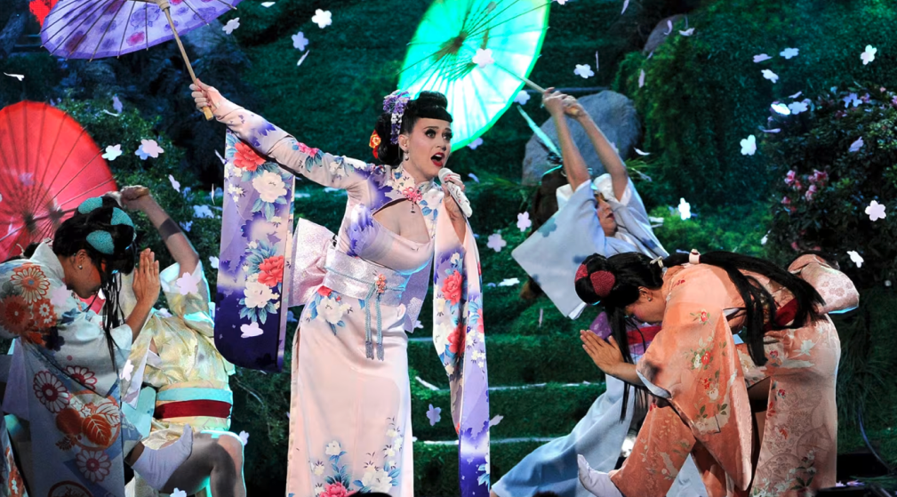 Katy Perry in einem Seidenkleid im Kimono-Stil mit tiefem Ausschnitt. Ein Outfit, das kulturelle Elemente der japanischen Geisha-Darstellung aufgreift und im Kontext kultureller Aneignung kritisiert wurde.